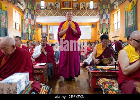 A Nepalese monk in traditional robes recites prayers & meditates with his hands clasped at the Sherpa Kyidug temple in Elmhurst, Queens, New York City Stock Photo