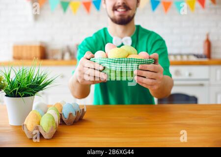 Happy Easter. A funny bearded man holds a basket with eggs and rabbit ears in the decorated room. Stock Photo