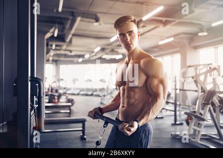 Muscular Fitness Bodybuilder Doing Heavy Weight Exercise For Biceps On Machine With Cable In The Gym. Stock Photo