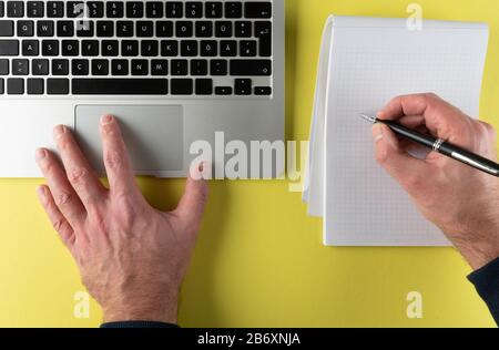 top view of person writing on notepad while working on laptop computer Stock Photo