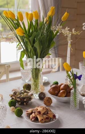 Easter festive spring table setting decoration, eggs in nest, fresh yellow tulips in vase, marshmallows, feathers, family dinner or breakfast concept, Stock Photo