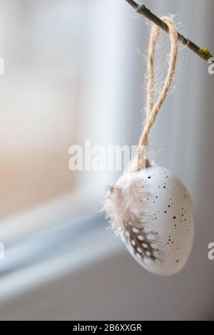 Easter egg with a feather hanging on tree branch, selective focus, home decoration background, copyspace Stock Photo
