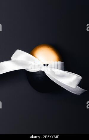 One black and golden Easter egg with bow on dark grey background. Flat lay, top view, copy space. Stock Photo