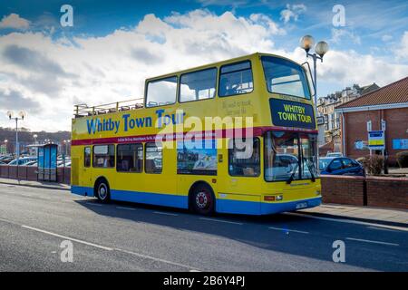 A bright yellow open topped double decker bus which takes tourists on a tour around the seaside town of Whitby Stock Photo