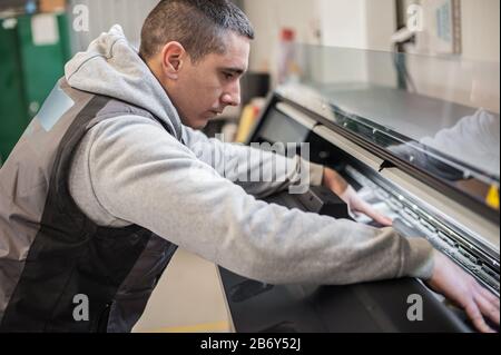 Technician worker operator changes the paper roll on large premium industrial printer and plotter machine in digital printshop office Stock Photo