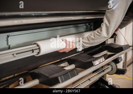 Technician worker operator changes the paper roll on large premium industrial printer and plotter machine in digital printshop office Stock Photo