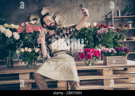Portrait of his he nice attractive cheerful cheery positive guy gardener sitting making selfie showing v-sign at modern industrial loft concrete style Stock Photo