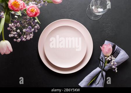Spring table setting with fresh pink tulips and pink decor on black stone table. Top view. Elegance dinner. Stock Photo