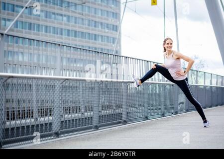 Junge Sportlerin macht Dehnübungen nach dem Sport in der Stadt. Young sportswoman does stretching exercises after sports in the city.