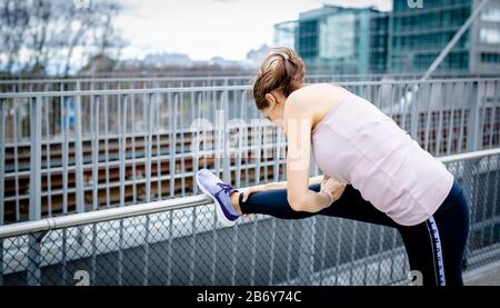 Junge Sportlerin macht Dehnübungen nach dem Sport in der Stadt. Young sportswoman does stretching exercises after sports in the city. Stock Photo