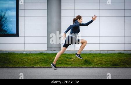 Sportlerin macht Sprintübungen / Startübung für den Sprint draußen in der Stadt. Athletic sportswoman does sprinting exercises outside in the city. Stock Photo
