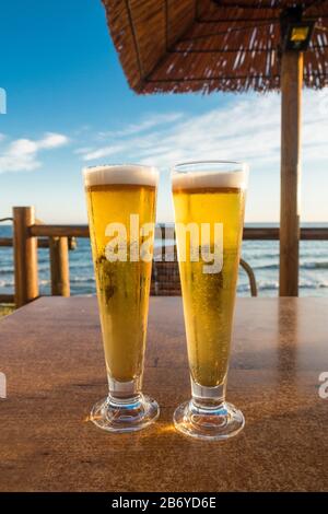 Two Glasses of beer on a table served in a beach restaurant, with mediterranean sea behind. Stock Photo