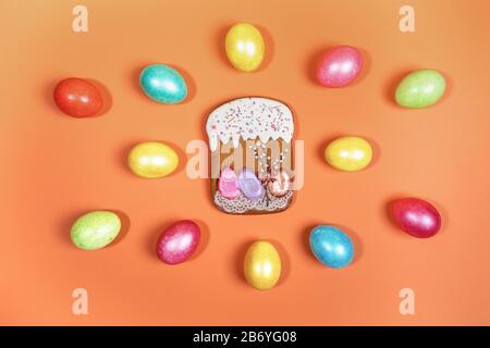 Festive Easter composition of bright multicolored eggs and gingerbread Easter cake on orange background. Painted eggs and Easter cake are Easter symbo Stock Photo