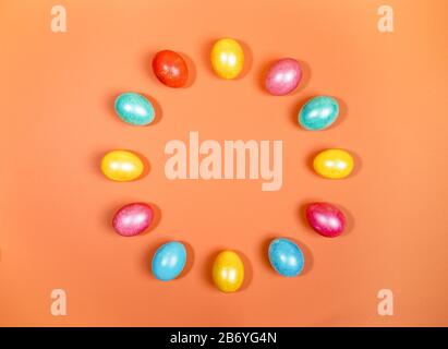 Bright multicolored glossy Easter eggs laid out in circle on trendy orange background. Creative festive Easter background. Painted eggs as symbols of Stock Photo