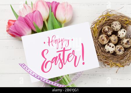 Easter greeting card with quail eggs in nest and tulip flowers over wooden background. Top view flat lay Stock Photo