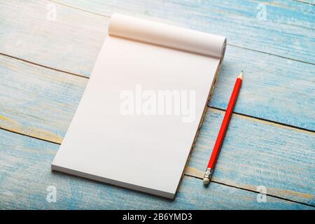 Notebook for writing with a red pencil on a blue background. Free empty space for writing on a blank sheet of a notebook, concept. Stock Photo