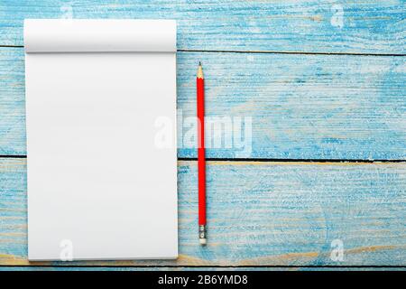 Notepad with red pencil on a blue wooden table background, for education, write goals and deeds. Free white space for writing on a blank sheet of note Stock Photo