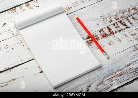 Notepad with a red pencil on a white wooden table against the background, for education, recording goals and deeds. Free white space for writing on a Stock Photo