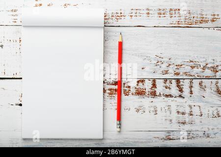 Notepad with a red pencil on a white wooden table against the background, for education, recording goals and deeds. Free white space for writing on a Stock Photo
