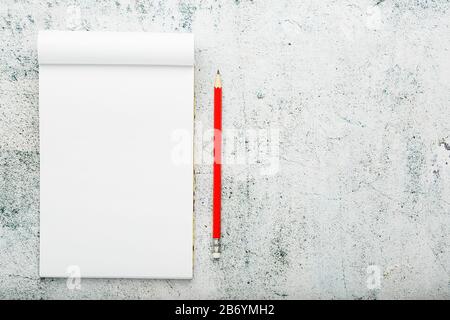 Notepad with red pencil on white plastered wall background, for education, write goals and deeds. Free white space for writing on a blank sheet of not Stock Photo