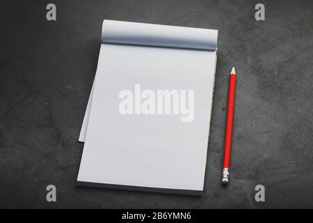 Notebook with a red pencil on a dark background for writing. Free empty space for writing on a blank sheet of a notebook, concept. Stock Photo
