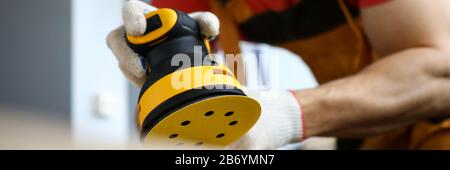 Male construction worker wearing hardhat and protective mask using sanding machine Stock Photo
