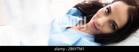 Sick woman lying at hospital bed with dropper in hand Stock Photo