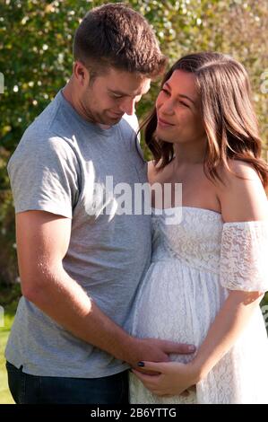 Beautiful pregnant young woman and her partner with their arms around each other Stock Photo