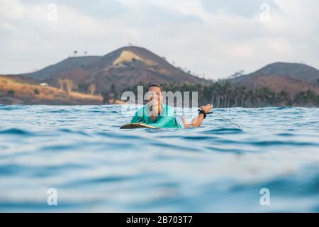 Smiling young woman lying on surfboard Stock Photo