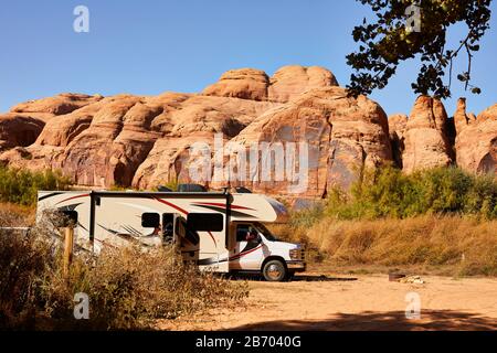An RV parked in front of a red rock wall in Moab, Utah. Stock Photo