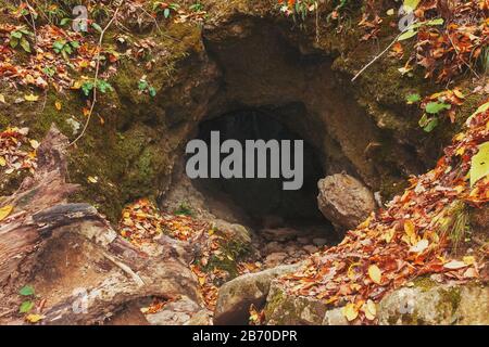 Large cave entrance in the autumn forest. Stock Photo