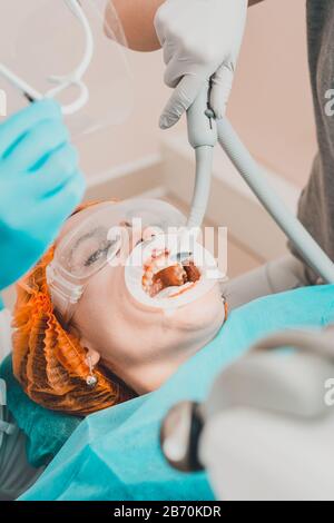 Dentist cleans teeth from stone using ultrasound, a woman sits in dental chair.2020 Stock Photo
