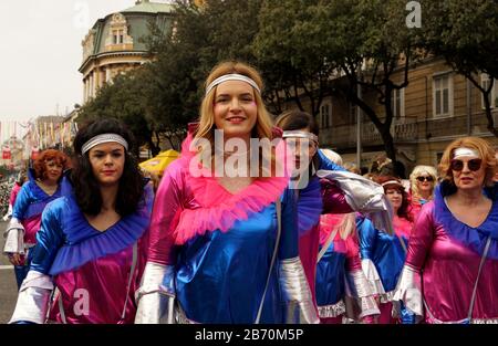 Rijeka, Croatia, February 23rd, 2020. Beautiful young and happy blonde girl smiling and walking in the center of the cheerful carnival group on the pa Stock Photo