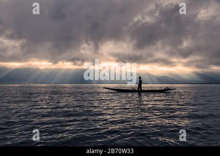 Burmese fisherman on bamboo boat catching fish in traditional way with handmade net. Inle lake, Myanmar (Burma) travel destination Stock Photo