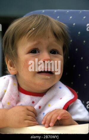 Austin Texas USA, 1995: Fussy one-year-old boy sits in high chair while eating breakfast.  MR  ©Bob Daemmrich Stock Photo