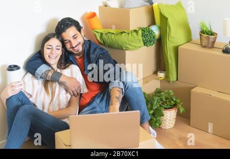 Happy young couple moving in new home first time - Man and woman having fun using computer next carton box in new property house Stock Photo