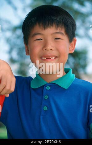 Austin, Texas USA: Young Asian-American boy missing his two front teeth poses for portrait outdoors. MR ©Bob Daemmrich Stock Photo