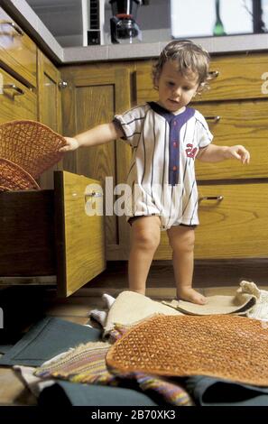 Austin Texas USA, 1995: 18-month-old toddler explores household items by taking placemats out of drawer, placing them on the floor, then putting them back in the drawer. MR ©B. Daemmrich Stock Photo