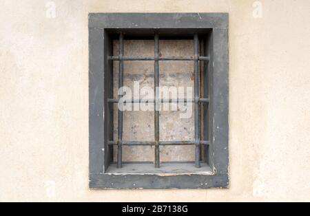 window with bars in the old city. there is one window on the wall which is closed and with a strong grating. prison in the city Stock Photo