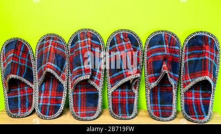 A lot of  of colorful comfortable, cushioned, checkered disposable slippers leaned against yellow wall. Close-up. Indoors. Stock Photo