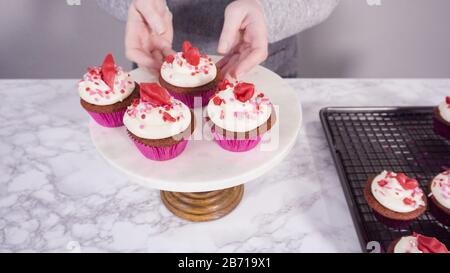 Step by step. Arranging red velvet cupcakes on a marble cake stand. Stock Photo