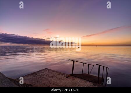 view of the evening sea from the pier, a ladder descends into the sea Stock Photo