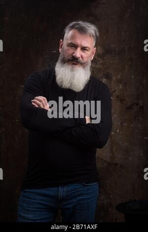 Studio portrait of handsome mature gray-haired bearded man against the dark wall, selective focus Stock Photo