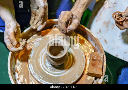 Professional potter makes a pot on a pottery wheel and teaches a pupil. Hands of a potter. Stock Photo