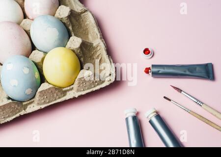 The concept of coloring Easter eggs in pastel watercolor colors. Paints and brushes for coloring eggs for Easter on pink background. Stock Photo