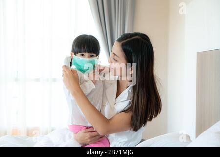 Asian young mother checking measurement temperature of her sick little daughter feel like fever or flu in bedroom at home. Visuals of people feeling s Stock Photo