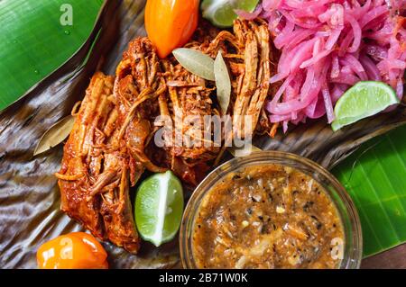 Cochinita Pibil, Mexican pit-roasted pork dish from Yucatan peninsula, served on banana leaves with traditional condiments Stock Photo