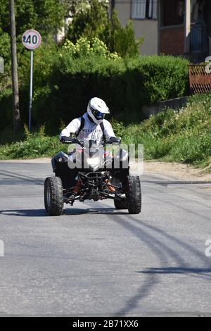 A quad driver in white drives down the street Stock Photo