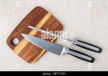Professional chef knife and a sharpening steel on wooden cutting board over a kitchen table. Kitchen utensils of high carbon molybdenum vanadium steel Stock Photo