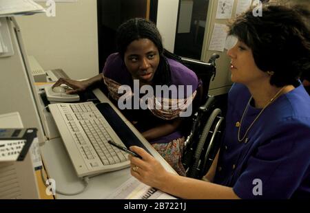 Austin Texas USA, 1994: Black woman in wheelchair and co-worker look at report on computer at their office.  MR   ©Bob Daemmrich Stock Photo